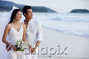 AsiaPix - Bride and groom standing on beach, holding hands, looking away