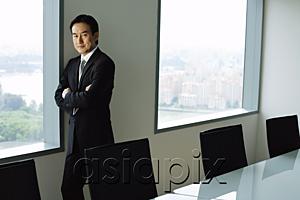 AsiaPix - Businessman standing next to window in conference room, looking at camera