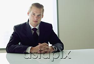 AsiaPix - Businessman sitting at table, hands clasped, looking at camera