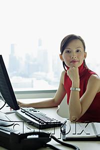 AsiaPix - Female executive sitting at office desk, looking at camera