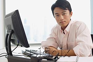 AsiaPix - Male executive sitting at office desk, looking at camera