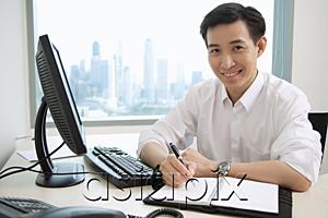 AsiaPix - Male executive sitting at office desk, looking at camera, smiling