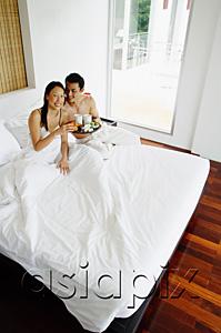 AsiaPix - Couple having breakfast in bed, woman smiling at camera, high angle view