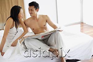 AsiaPix - Couple sitting on bed with newspaper, looking at each other