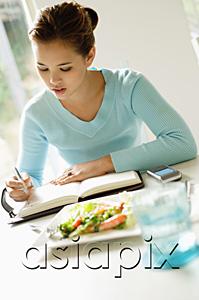 AsiaPix - Young woman sitting at table, food next to her, writing in notebook