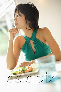 AsiaPix - Young woman at table, looking away, plate of salad in front of her