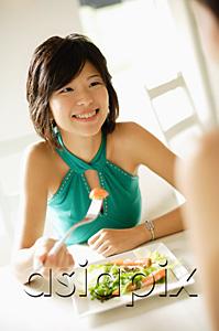 AsiaPix - Young woman at table, eating salad, smiling at person in front of her