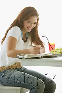 AsiaPix - One woman sitting at table, writing in notebook, smiling