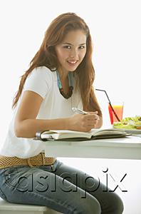 AsiaPix - One woman sitting at table, writing in notebook, smiling at camera