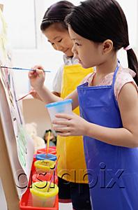 AsiaPix - Young girls in blue and yellow aprons painting on easel