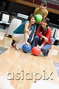 AsiaPix - Three women crouching in bowling alley, holding bowling balls