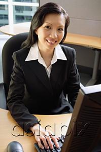 AsiaPix - Businesswoman sitting at desk, using computer, smiling at camera
