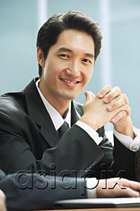 AsiaPix - Businessman smiling at camera, hands clasped