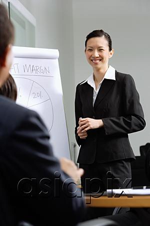 AsiaPix - Businesswoman standing next to flipchart, smiling at colleagues