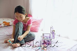 AsiaPix - Girl in T shirt and jeans sitting on bed, painting toenails