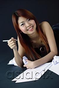 AsiaPix - Woman holding crumpled paper and pen, smiling at camera