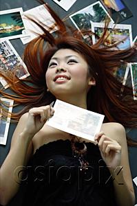 AsiaPix - Woman lying on floor, pictures spread around her, holding postcard