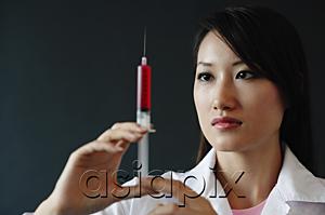 AsiaPix - Female doctor looking at syringe, serious expression