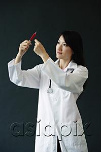 AsiaPix - Female doctor standing, looking at syringe