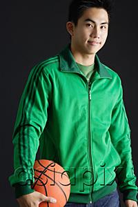 AsiaPix - Young man wearing green tracksuit jacket, holding basketball, looking at camera
