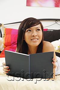AsiaPix - Girl lying on bed, holding diary, looking away
