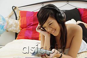 AsiaPix - Girl lying on bed, holding CD case, listening to headphones