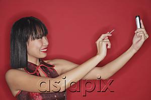 AsiaPix - Woman standing against red background, using PDA