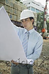 AsiaPix - Businessman wearing hardhat, looking at blueprints