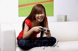 AsiaPix - Young woman sitting on sofa, holding TV remote control