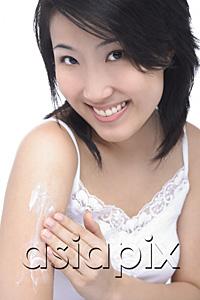 AsiaPix - Young woman applying moisturizer on arm, smiling at camera
