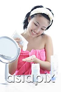 AsiaPix - Young woman sitting at dressing table, putting moisturizer on hand