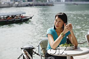 AsiaPix - Young woman sitting at riverside cafe, looking away, smiling