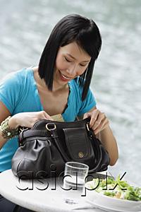 AsiaPix - Young woman sitting at riverside cafe, looking through her handbag