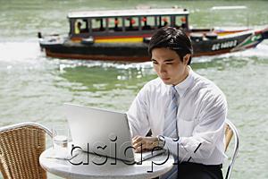 AsiaPix - Businessman sitting at outdoor cafe, using laptop, river in the background