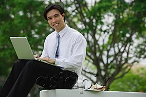 AsiaPix - Businessman sitting in park with laptop, looking at camera
