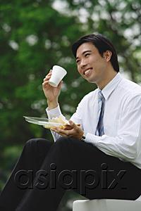 AsiaPix - Young businessman sitting outdoors, having lunch