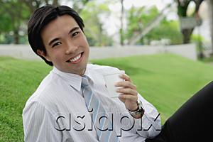 AsiaPix - Businessman sitting in park, holding disposable cup