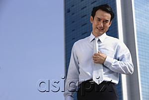 AsiaPix - Businessman standing looking at camera, hand on tie