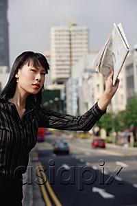 AsiaPix - Businesswoman hailing a taxi with newspaper in hand