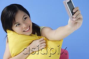 AsiaPix - Young woman hugging pillow, using mobile phone to take a picture