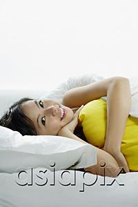 AsiaPix - Young woman lying on bed, embracing pillow