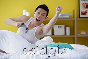 AsiaPix - Man sitting in bed, holding video game remote control, arms outstretched