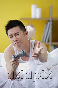AsiaPix - Man lying on bed, playing video game, making a face