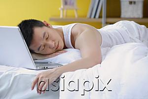 AsiaPix - Man lying on bed, sleeping, laptop next to him