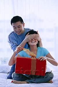 AsiaPix - Couple in bedroom, woman opening gift, man covering her eyes