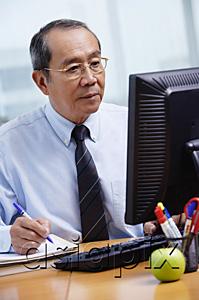 AsiaPix - Businessman sitting at his desk, looking at computer