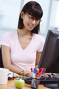 AsiaPix - Young woman sitting at desk, looking at computer