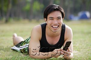 AsiaPix - Man lying on grass, holding mobile phone