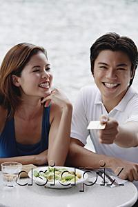 AsiaPix - Couple sitting at outdoor cafe, man holding credit card towards camera
