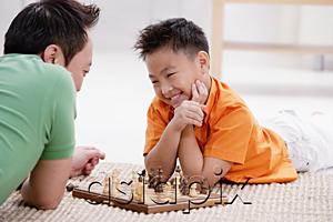 AsiaPix - Father and son lying on floor, playing chess, smiling